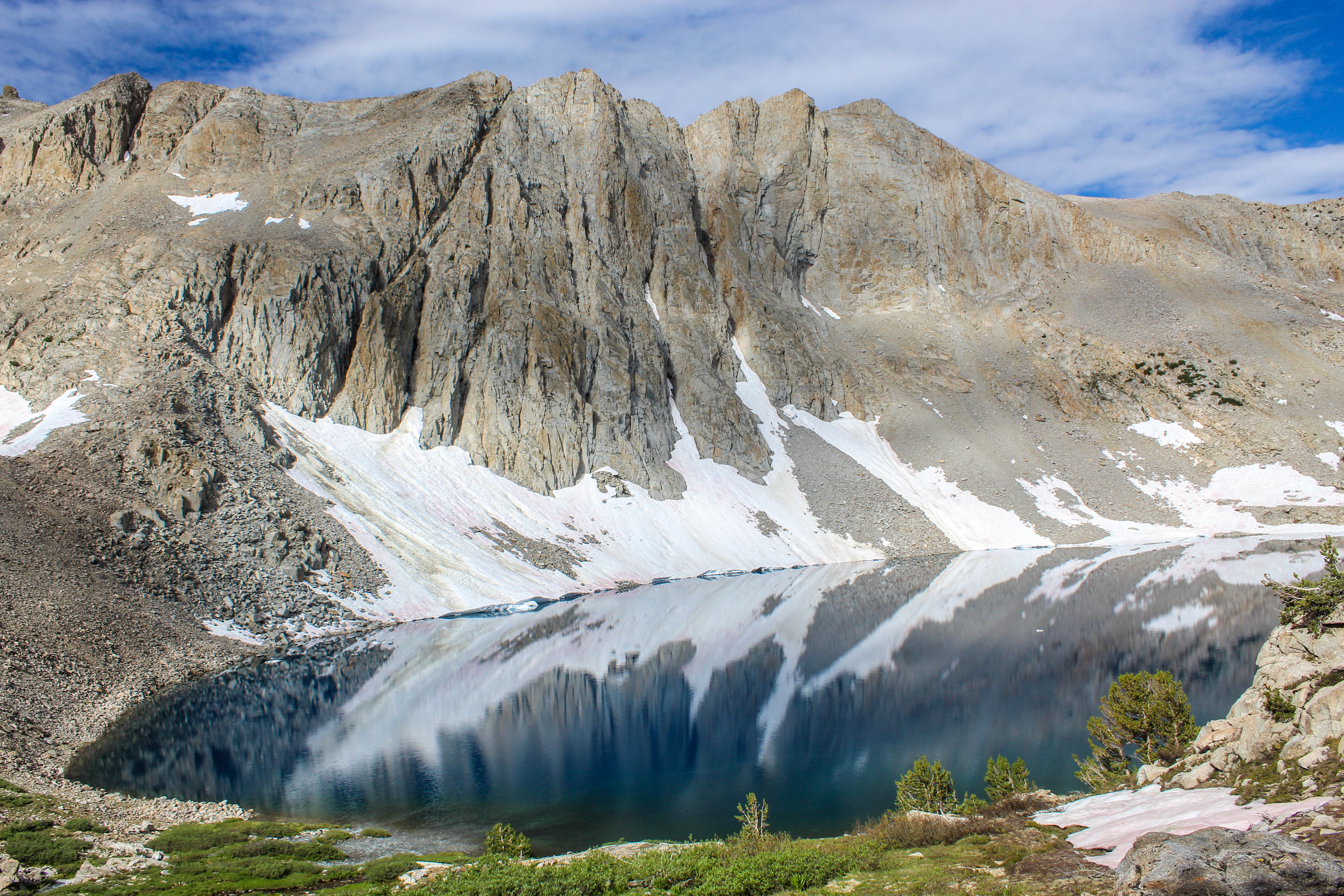 An alpine lake perfectly mirrors the stark, stone-faced mountain above.